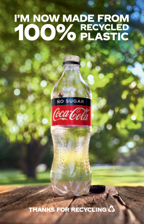 Empty coke bottle against nature background with "I'M NOW MADE FROM 100% RECYCLED PLASTIC" text