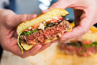 Impossible Meat burger 2.0 cut in half and held by two hands
