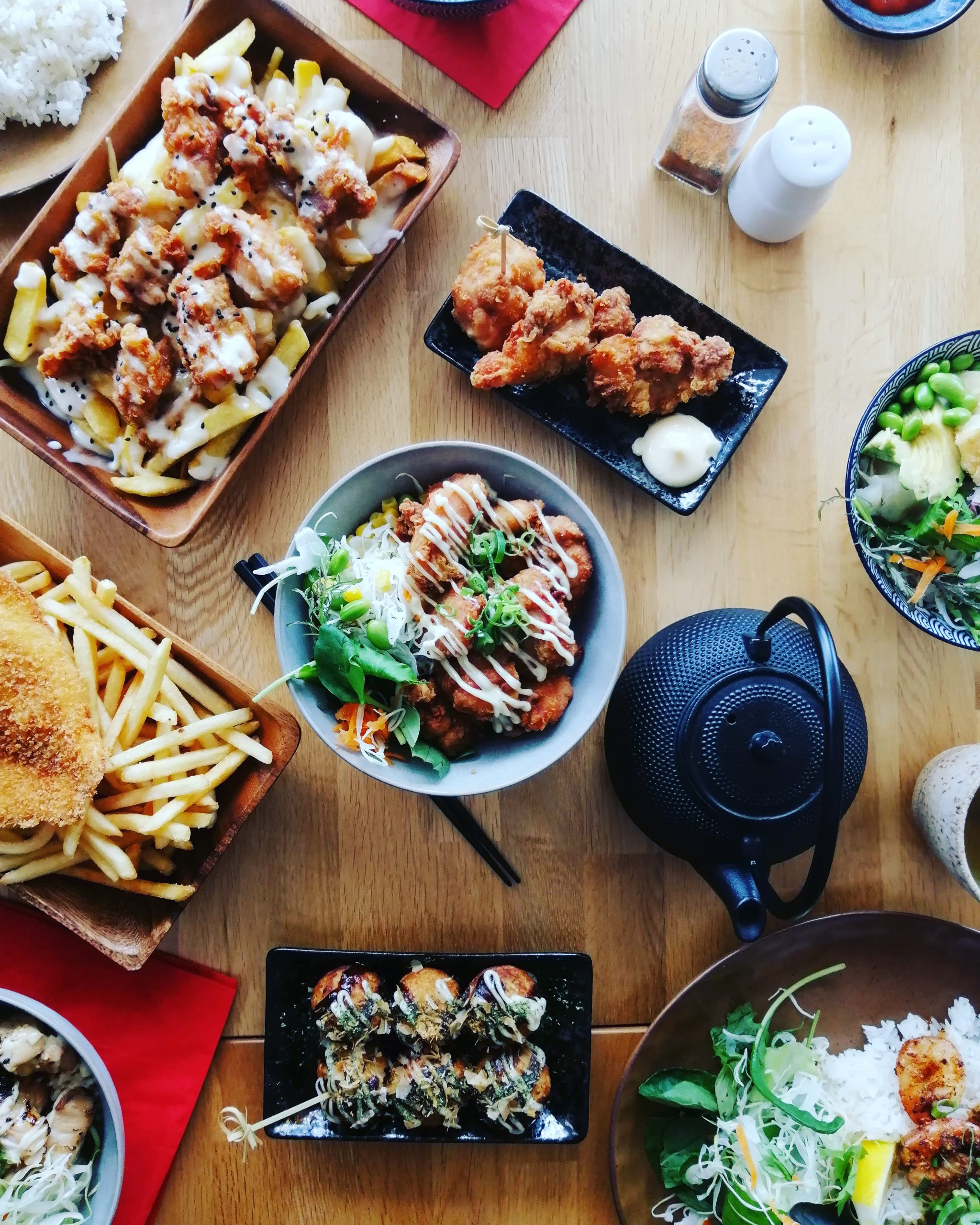 table of assorted dishes, fried katsu chicken, sushi, salad, tea pot, salt and pepper, fries