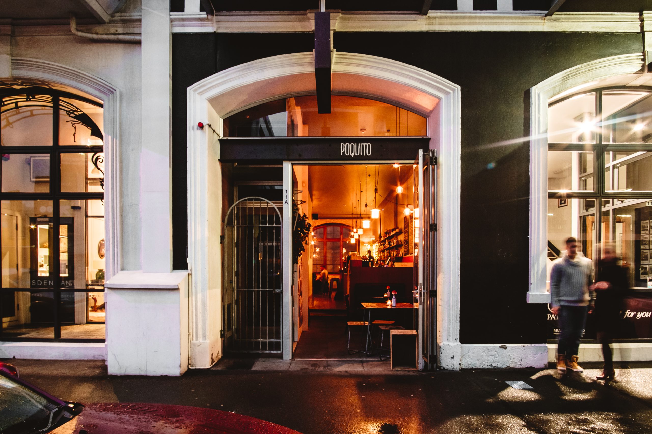 POquito bar at night with entrance and sign and warm light shining through door way