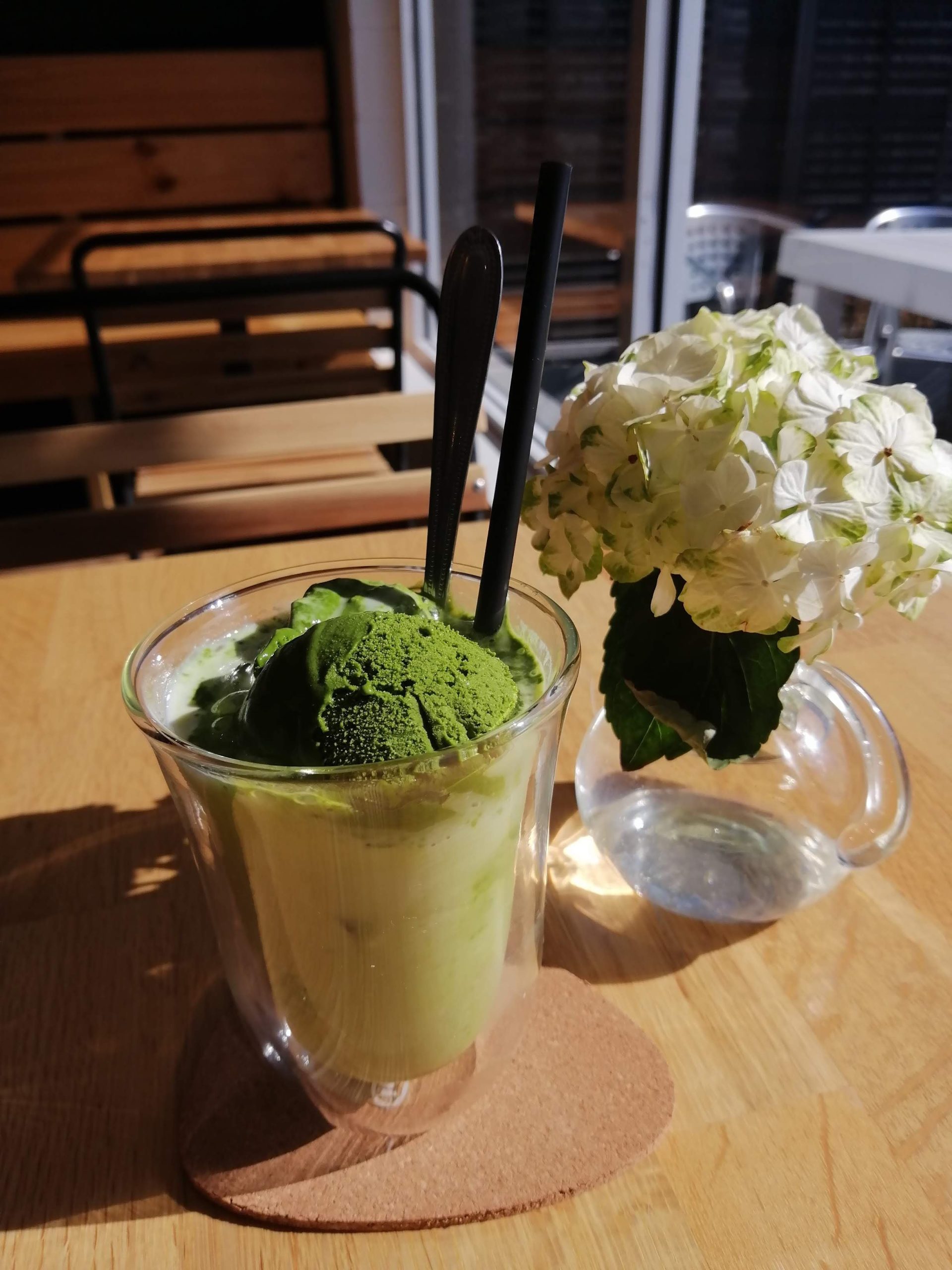 glass of matcha icecream on coaster placed on table with a white hydrangea in vase next to it