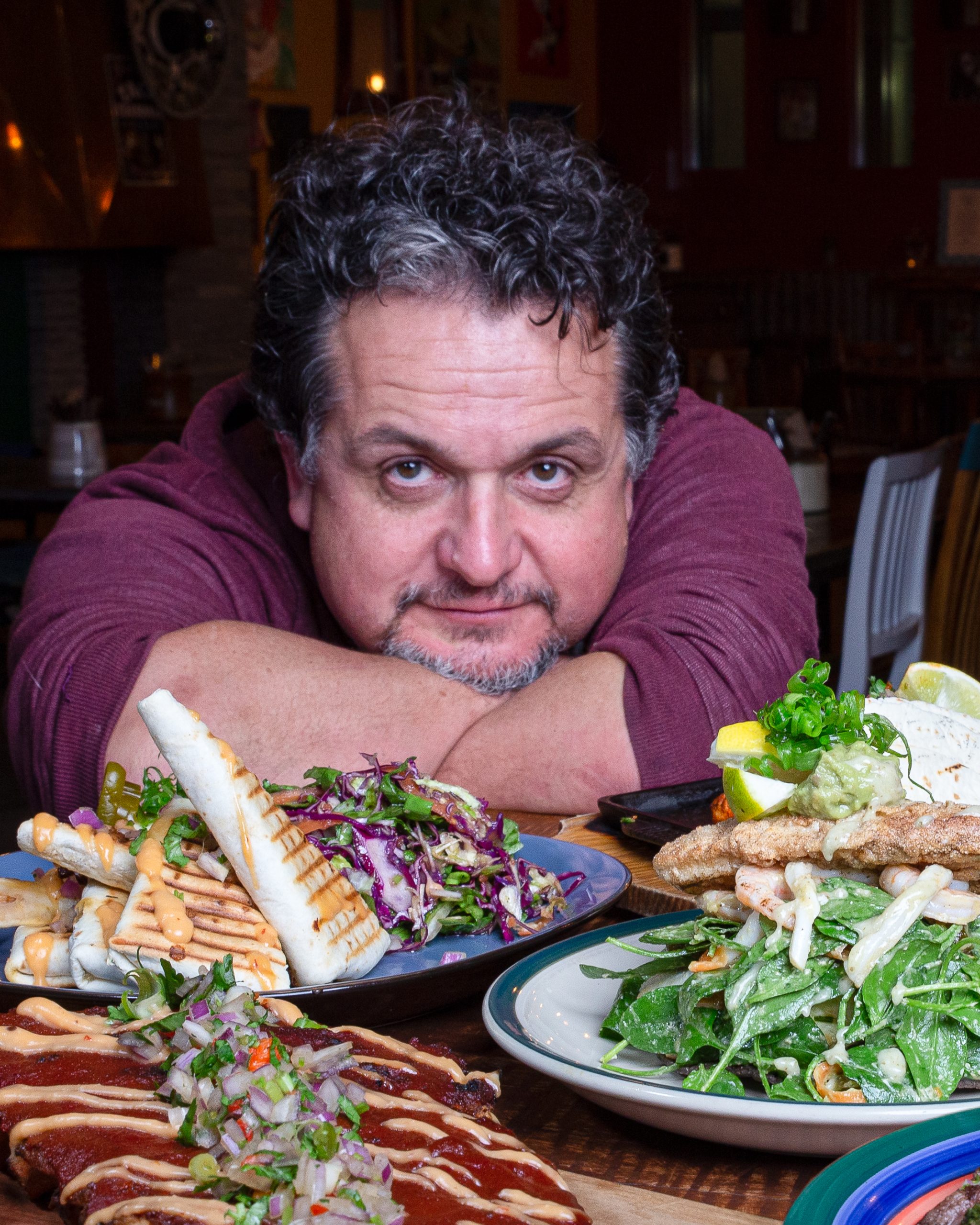 Chef male perched over table with dishes of mexican food in front of him