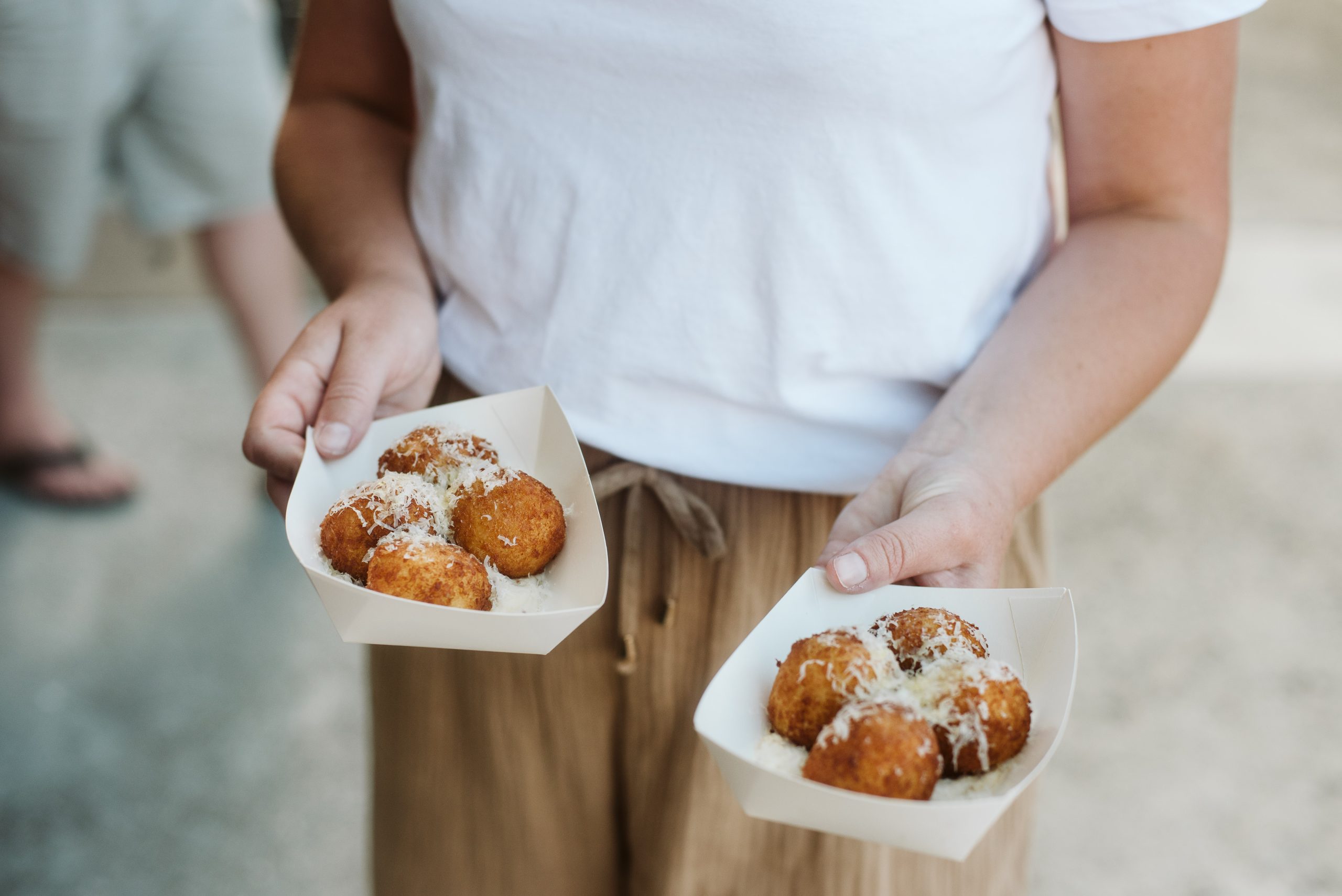 torso of ownder holding two street food dishes in either hand arancini balls with grated cheese on top