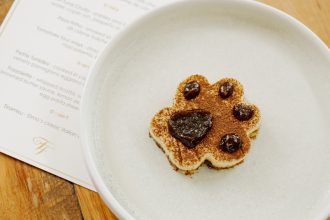 Tiramisu in the shape of a pawprint sits in the center of a white plate on a wooden table.